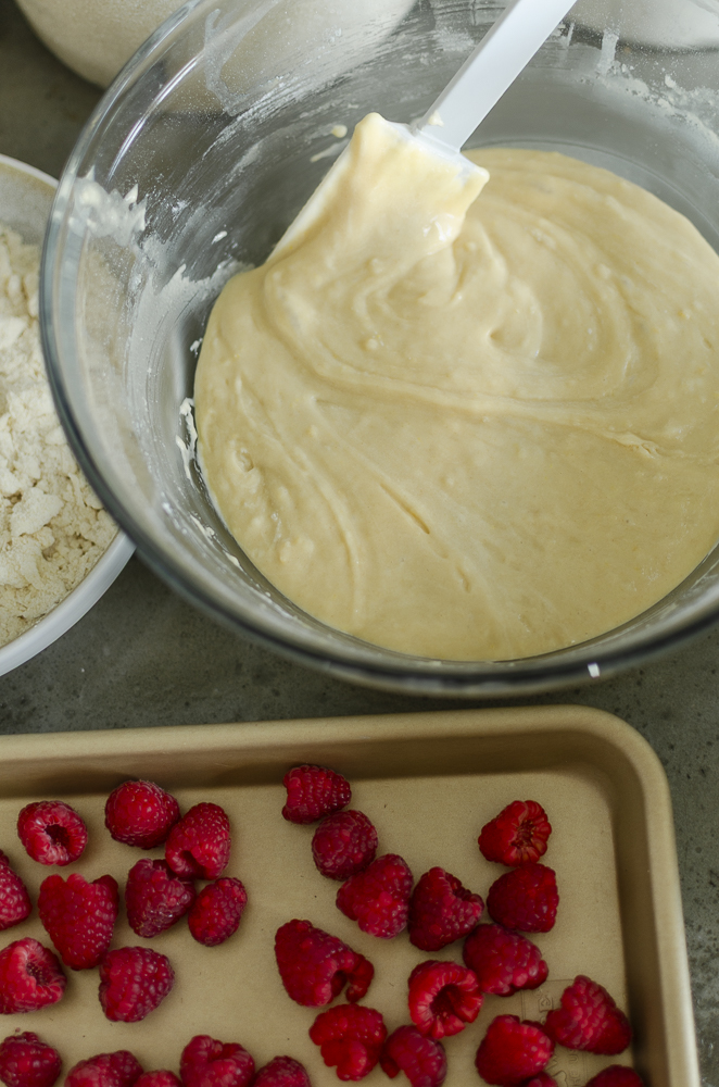 lemon raspberry muffin batter in a bowl next to a cookie sheet of raspberries