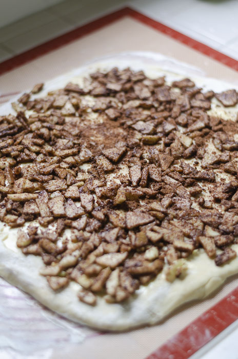 sourdough apple cinnamon roll dough rolled out on a mat and topped with apple filling